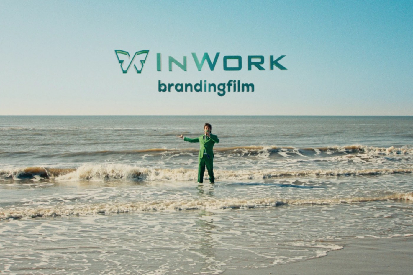 Still uit de brandingfilm van InWork: een man in een groen pak staat zingend in de branding, met de titel InWork brandingfilm in de lucht.